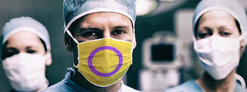 Three surgeons, one of who is wearing a mask with the intersex flag.