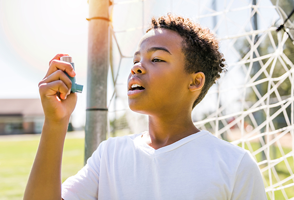 Child outside on soccer field in front of the goal post using an inhaler.