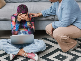 Full length portrait of depressed teenage girl sitting on floor with mother or therapist trying to communicate