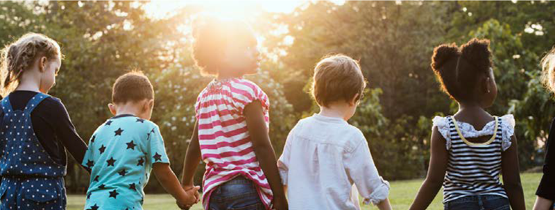 Children holding hands in front of a sunset.