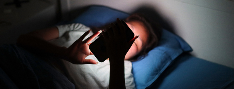 Girl lying in bed using mobile phone late at night in the dark