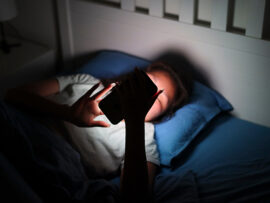 Girl lying in bed using mobile phone late at night in the dark